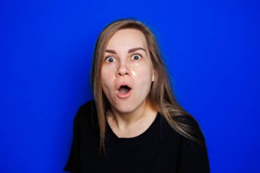 Cute young blonde woman with natural smooth skin without makeup posing happy and smiling at camera while standing in t-shirt on blue background. Beauty concept, eye patches for women