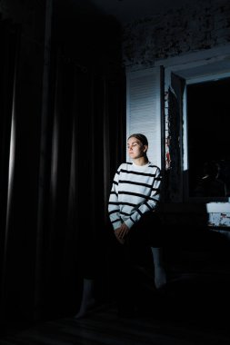 Cute stylish young woman in black leggings and striped jumper sitting on sofa. Women's fashion, women's casual style.