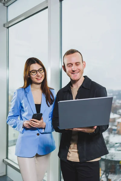 Two business people working remotely online using a laptop. Colleagues work in the workspace remotely standing near the window.