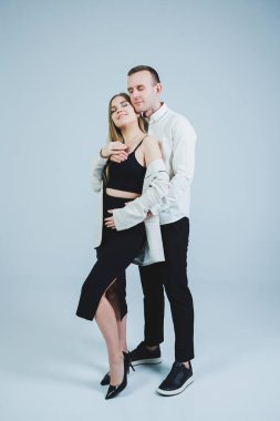 Happy young man standing with his pregnant wife and hugging her belly, isolated on white background. Stylish young people. A man in a shirt and a woman in a black skirt and jacket
