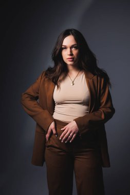 Stylish pretty young woman in brown classic suit sitting on gray background. Beautiful woman in a jacket and with makeup on her face