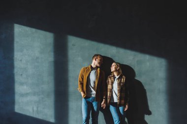 A young married couple in love in shirts and jeans on the background of a gray wall. The concept of happy family relationships. A man and a woman are hugging