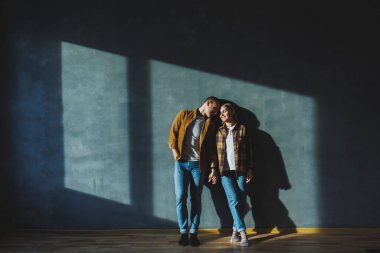 Happy couple in love dressed in shirts, standing on the background of gray wall, looking at empty space, isolated background of gray concrete wall. The concept of a happy couple in love.