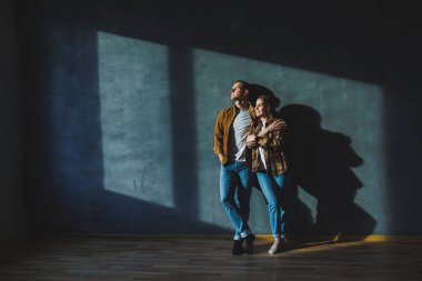 Smiling happy couple dressed in jeans and shirts standing on a gray wall background, isolated gray concrete wall background. The concept of a happy couple in love.