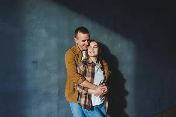 Happy couple in love dressed in shirts, standing on the background of gray wall, looking at empty space, isolated background of gray concrete wall. The concept of a happy couple in love.