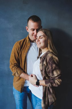 Smiling happy couple dressed in jeans and shirts standing on a gray wall background, isolated gray concrete wall background. The concept of a happy couple in love.