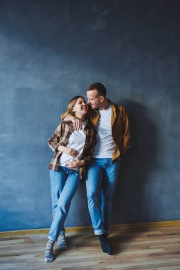 Happy couple in love dressed in shirts, standing on the background of gray wall, looking at empty space, isolated background of gray concrete wall. The concept of a happy couple in love.