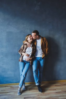 A young married couple in love in shirts and jeans on the background of a gray wall. The concept of happy family relationships. A man and a woman are hugging