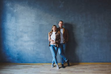 A young married couple in love in shirts and jeans on the background of a gray wall. The concept of happy family relationships. A man and a woman are hugging