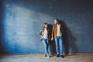 Happy couple in love dressed in shirts, standing on the background of gray wall, looking at empty space, isolated background of gray concrete wall. The concept of a happy couple in love.