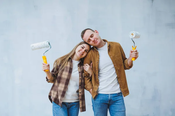 A young married couple in love paints the walls with white paint using rollers. Renovation in the apartment of a happy couple