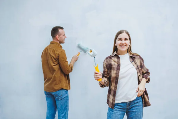 Young married couple in love in shirts and jeans doing renovations, renewing painting walls with a roller, preparing to move into a new house, selective focus