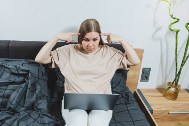 Satisfied young woman finishing work on laptop. European girl sitting with computer in bed, studying at home, distance learning and remote freelance work concept