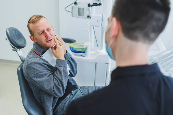 stock image A young dentist doctor tells a male patient about dental care. A man was sitting in a dental chair at a doctor's appointment. Modern dental treatment