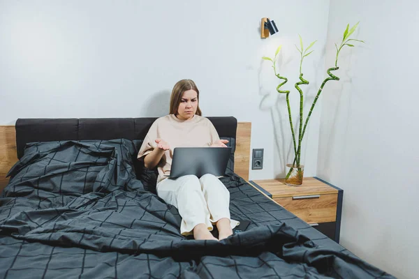 stock image Satisfied young woman finishing work on laptop. European girl sitting with computer in bed, studying at home, distance learning and remote freelance work concept