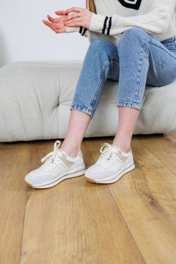Close-up of female legs in jeans and casual sneakers. Women's comfortable casual shoes. White leather women's sneakers