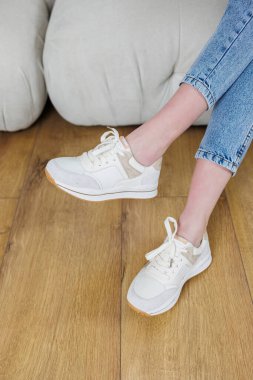 Close-up of female legs in jeans and casual sneakers. Women's comfortable casual shoes. White leather women's sneakers