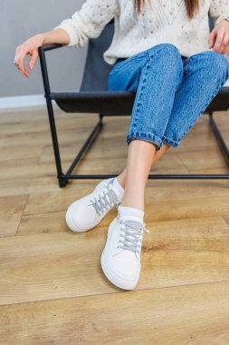 Close-up of female legs in jeans and casual white sneakers. Women's comfortable casual shoes. White leather women's sneakers