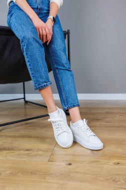 Close-up of female legs in jeans and casual white sneakers. Women's comfortable casual shoes. White leather women's sneakers
