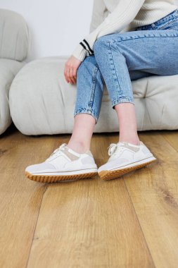 Close-up of female legs in jeans and casual sneakers. Women's comfortable casual shoes. White leather women's sneakers