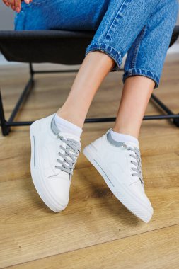 Close-up of female legs in jeans and casual white sneakers. Women's comfortable casual shoes. White leather women's sneakers