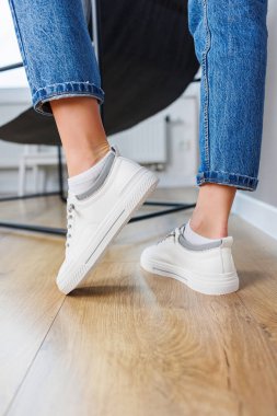 Close-up of female legs in jeans and casual white sneakers. Women's comfortable casual shoes. White leather women's sneakers