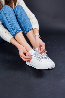Close-up of female legs in jeans and casual white sneakers. Women's comfortable casual shoes. White leather women's sneakers