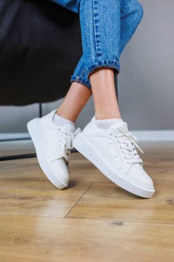 Close-up of female legs in jeans and casual white sneakers. Women's comfortable casual shoes. White leather women's sneakers