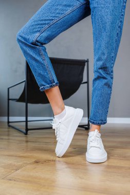 Close-up of female legs in jeans and casual white sneakers. Women's comfortable casual shoes. White leather women's sneakers