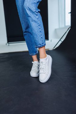 Close-up of female legs in jeans and casual white sneakers. Women's comfortable casual shoes. White leather women's sneakers