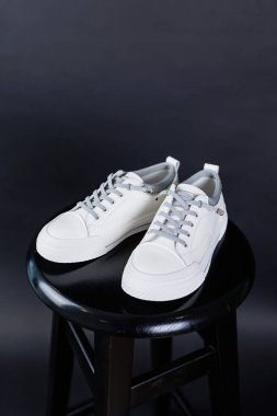 Women's white leather sneakers close-up on a black background. Women's everyday comfortable shoes.
