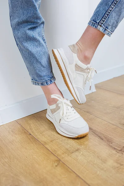 Close-up of female legs in jeans and casual sneakers. Women\'s comfortable casual shoes. White leather women\'s sneakers