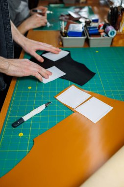 Atölyesinde deri cüzdan için deri parçaları tutan bir adam. Doğal kahverengi deri ile çalışma süreci. Zanaatkar zanaatı elinde tutar.