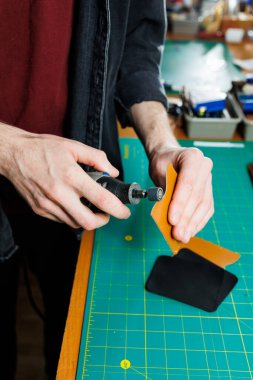 Atölyesinde deri cüzdan için deri parçaları tutan bir adam. Doğal kahverengi deri ile çalışma süreci. Zanaatkar zanaatı elinde tutar.