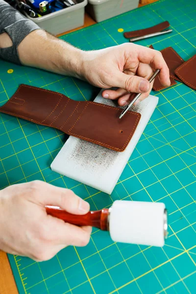 A man\'s hand holds pieces of leather for a leather wallet in his workshop. The process of working with natural brown leather. The craftsman holds the craft