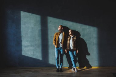 A young married couple in love in shirts and jeans on the background of a gray wall. The concept of happy family relationships. A man and a woman are hugging