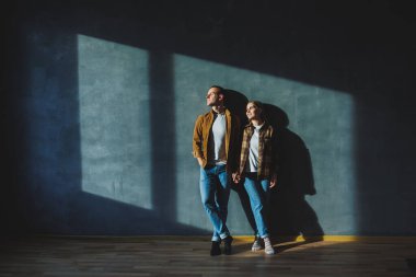 Happy couple in love dressed in shirts, standing on the background of gray wall, looking at empty space, isolated background of gray concrete wall. The concept of a happy couple in love.