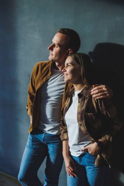 Smiling happy couple dressed in jeans and shirts standing on a gray wall background, isolated gray concrete wall background. The concept of a happy couple in love.