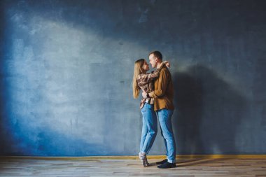 Smiling happy couple dressed in jeans and shirts standing on a gray wall background, isolated gray concrete wall background. The concept of a happy couple in love.