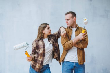 A young married couple in love paints the walls with white paint using rollers. Renovation in the apartment of a happy couple