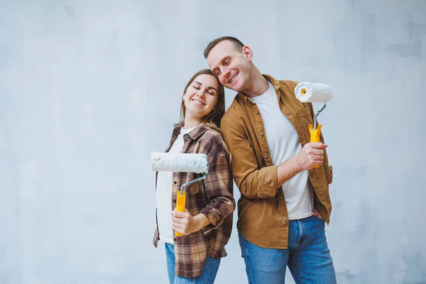A young married couple in love paints the walls with white paint using rollers. Renovation in the apartment of a happy couple