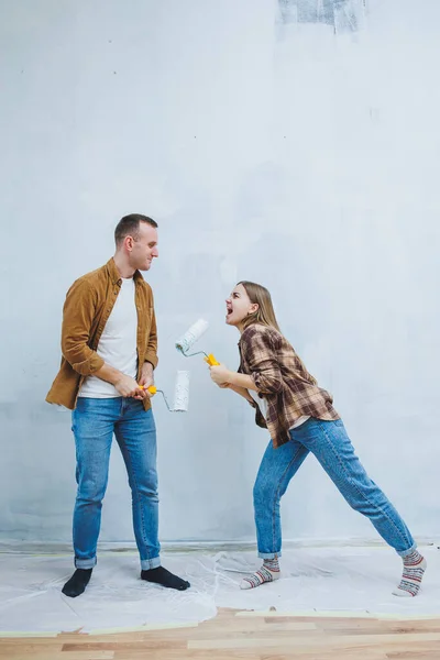 Couple in love, newlyweds in shirts and jeans in an empty room, painting white walls and renovating the interior. A man and a woman moved to a new house. Selective focus
