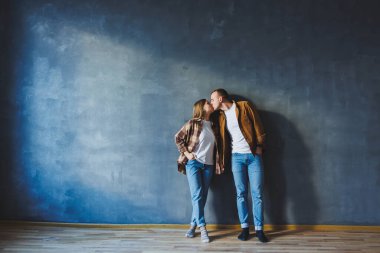 A young married couple in love in shirts and jeans on the background of a gray wall. The concept of happy family relationships. A man and a woman are hugging