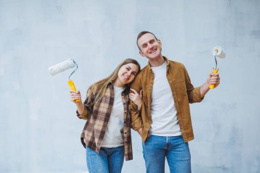 A young married couple in love paints the walls with white paint using rollers. Renovation in the apartment of a happy couple