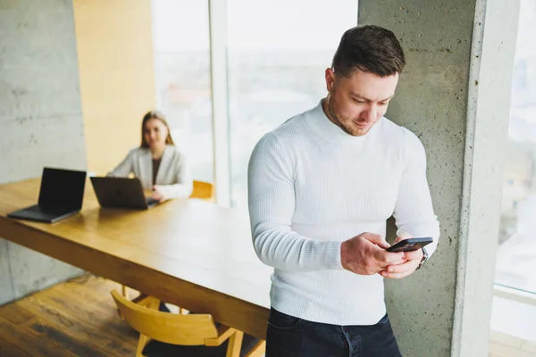 stock image Successful male businessman in casual clothes smiling looking at phone standing in modern light office with phone working in modern company.