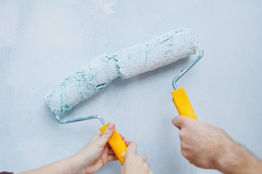 Couple in love, newlyweds in shirts and jeans in an empty room, painting white walls and renovating the interior. A man and a woman moved to a new house. Selective focus