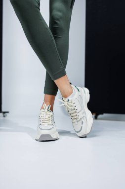 Deri taytlı ince kadın bacakları ve beyaz şık spor ayakkabıları. Kadınların rahat yaz ayakkabıları..