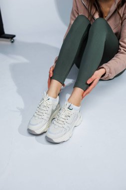 Deri taytlı ince kadın bacakları ve beyaz şık spor ayakkabıları. Kadınların rahat yaz ayakkabıları..