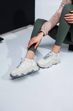 Deri taytlı ince kadın bacakları ve beyaz şık spor ayakkabıları. Kadınların rahat yaz ayakkabıları..