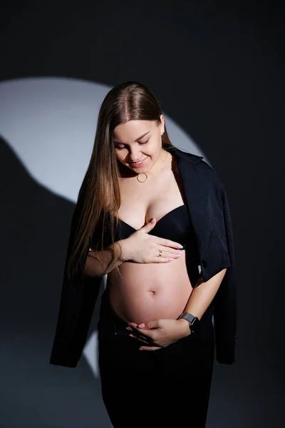 灰色の背景に黒いスーツを着た幸せな妊婦 美しいエレガントな妊婦さん 妊婦の優しいスタジオ写真 — ストック写真